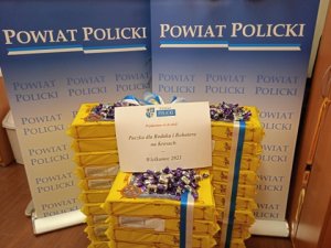Paczki cukierków w trzech kolumnach na tle roll upów z napisem POWIAT POLICKI przygotowane do przekazania na akcję Paczka dla Rodaka i Bohatera na Kresach-Wielkanoc 2021