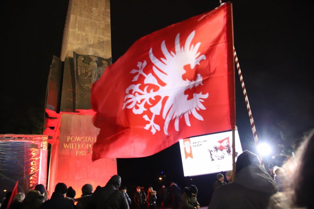 Pomnik upamietniający Powstanie Wielkopolskie w tle choragiew symbol wydarzenia - orzeł na czerwonym tle.