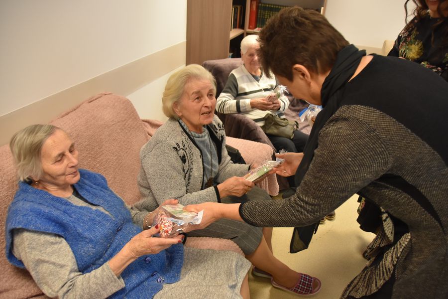 Na sofie siedzą dwie kobiety, którym wręczane zostają upominki od Członka Zarządu Powiatu w Policach Beaty Chmielewskiej