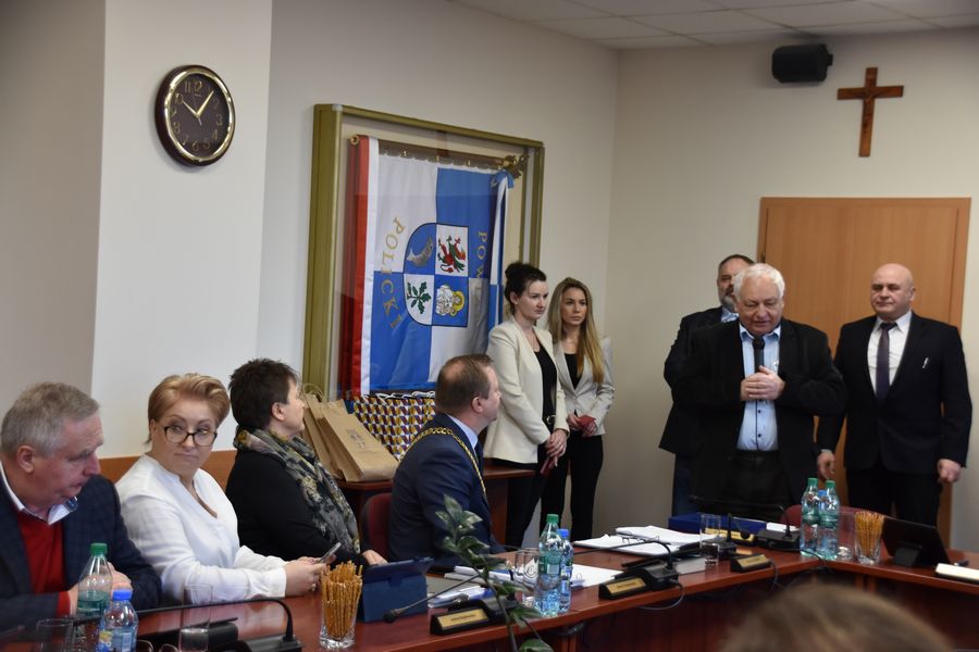 Obrady sesji Rady Powiatu w Policach, przy stole zasiadają radni Powiatu Polickiego, słuchają przemówienia stojącego męźczyzny z mikrofonem-Przewodniczącego Okręgowej Rady,za nim stoją dwie kobiety i dwóch mężczyzn