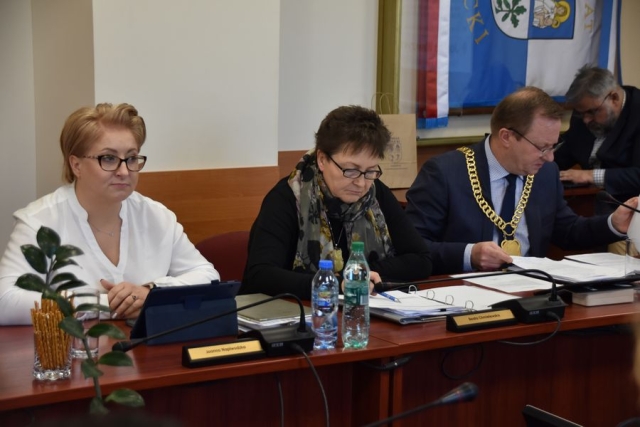 Podczas obrad sesji Rady Powiatu w Policach przy stole na krzesłach siedzi Zarząd Powiatu w Policach, czyli dwie kobiety i jeden męźczyzna