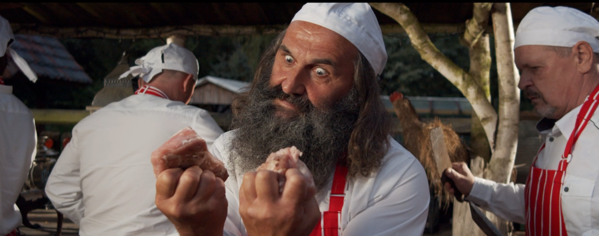 Kadr z teledysku brodaty mężczyzna - rzeźnik trzymający w dłoniach kawałki czerwonego mięsa.