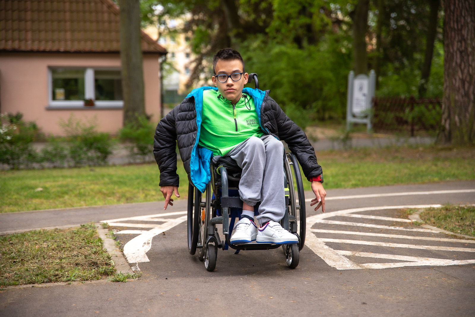 Chłopczyk w widocznej zielonej bluzie poruszający się wózkiem po drodze