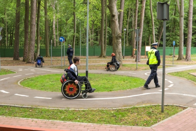 Trzy osoby poruszakjące się na wózku inwalidzkim w obecności dwóch policjantów na przyszykowanym specjalnie rondzie.
