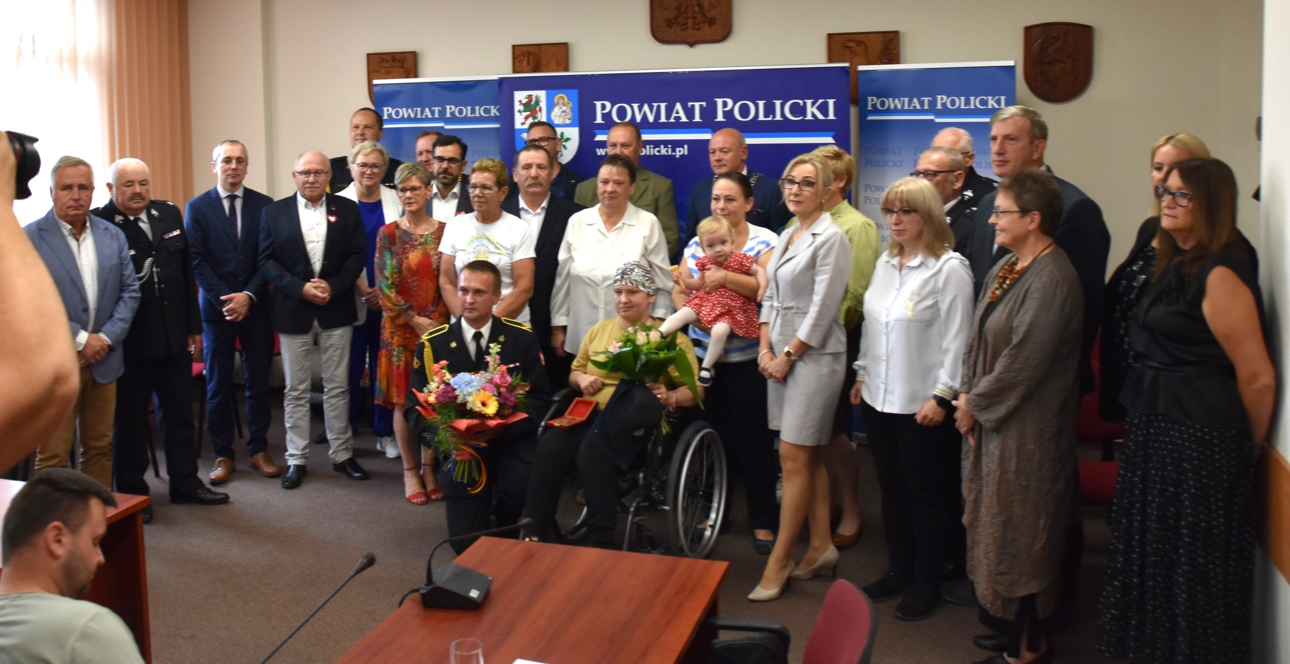 Zdjęcie grupowe z zaproszonym gościem na tle ścianki Powiat Polickiego.
