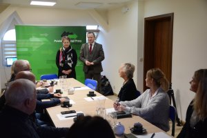 Dwie postacie stoją w tle. Z przodu siedzące osoby