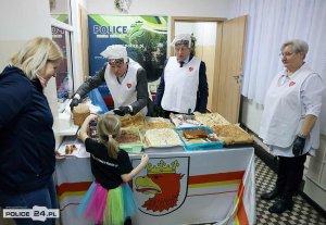 Dwóch mężczyzn w białych fartuchach przy stole oraz dziecko i dwie kobiety