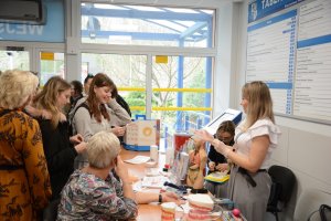 Stojący ludzie, pomiędzy nimi stoły z rzeczmi