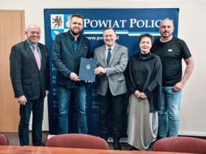 pięć osób stojących, w tle element reklamowy