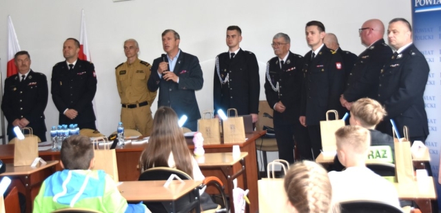 Członek Zarządu Powiatu w Policach przemawiający przez mikrofon do uczestników konkursu pożarniczego