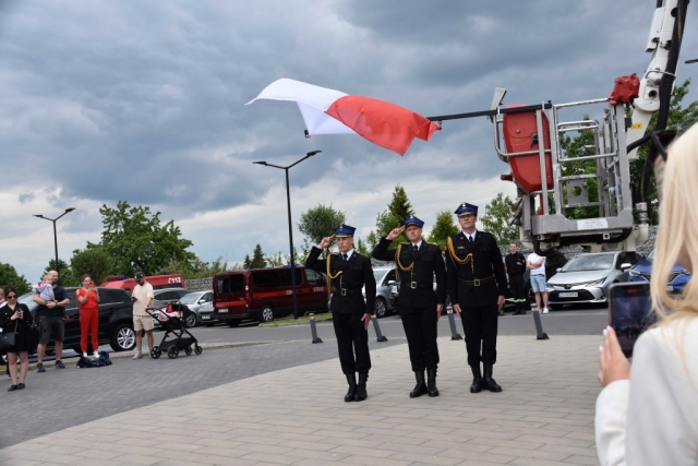Strażacy z zawieszoną i podniesioną flagą Polski