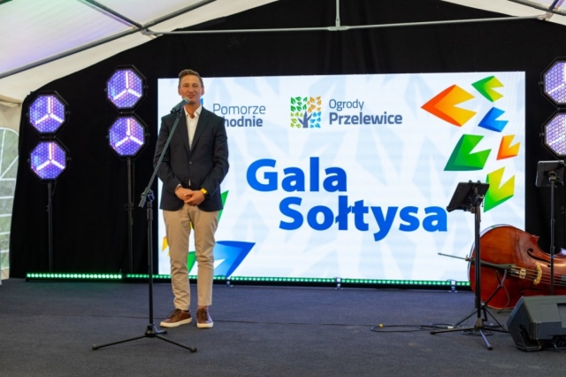 Na scenie, do mikrofonu przemawia Marszałek Województwa Zachodniopomorskiego, w tle grafika Gala Sołtysa