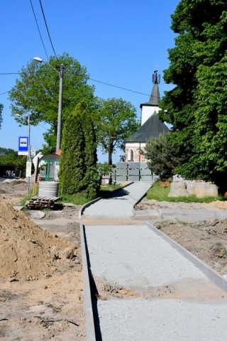 Remont drogi, trwające budowy chodników,w tle wieżyczka kościoła i drzewa