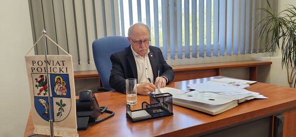 Janusz Szwyd Przewodniczący Rady Powiatu w Policach w trakcie podpisywania dokumentów, siedzący przy biurku w swoim gabinecie