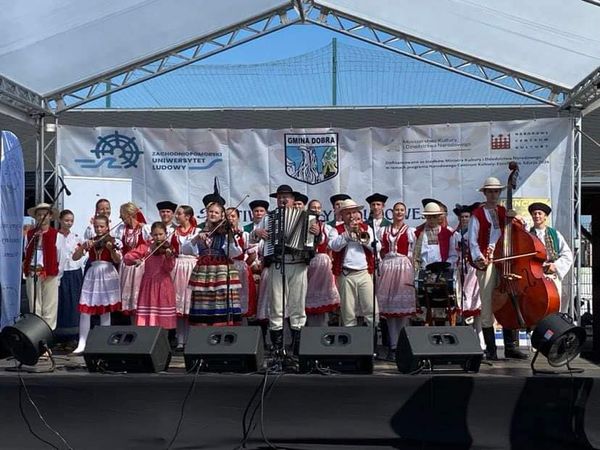 Zespół kilkunastoosobowy występujący na scenie w strojach ludowych.