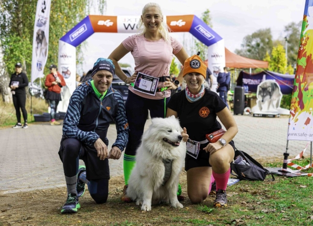 Grupowe zdjęcie sportowców pozujących z uśmiechem obok psa