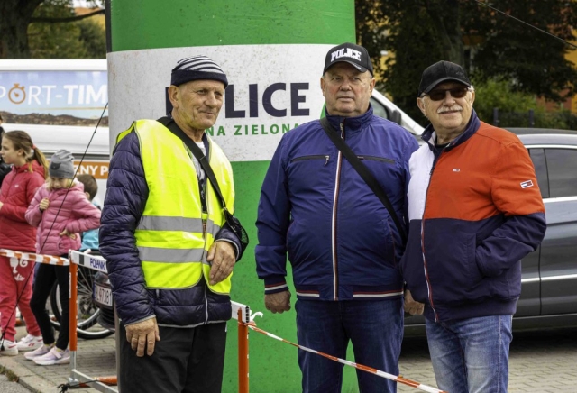 Przewodniczący Rady Powiatu w Policach stoi z uśmiechem, obserwując uczestników biegu